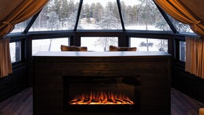 A cozy cabin interior with a fireplace, wooden walls, and a window offering a snowy forest view. - Wilderness Hotel Nellim & Igloos (Inari)