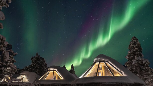 A snowy landscape with several wooden cabins, each with a triangular roof and a visible interior light. - Wilderness Hotel Nellim & Igloos (Inari)