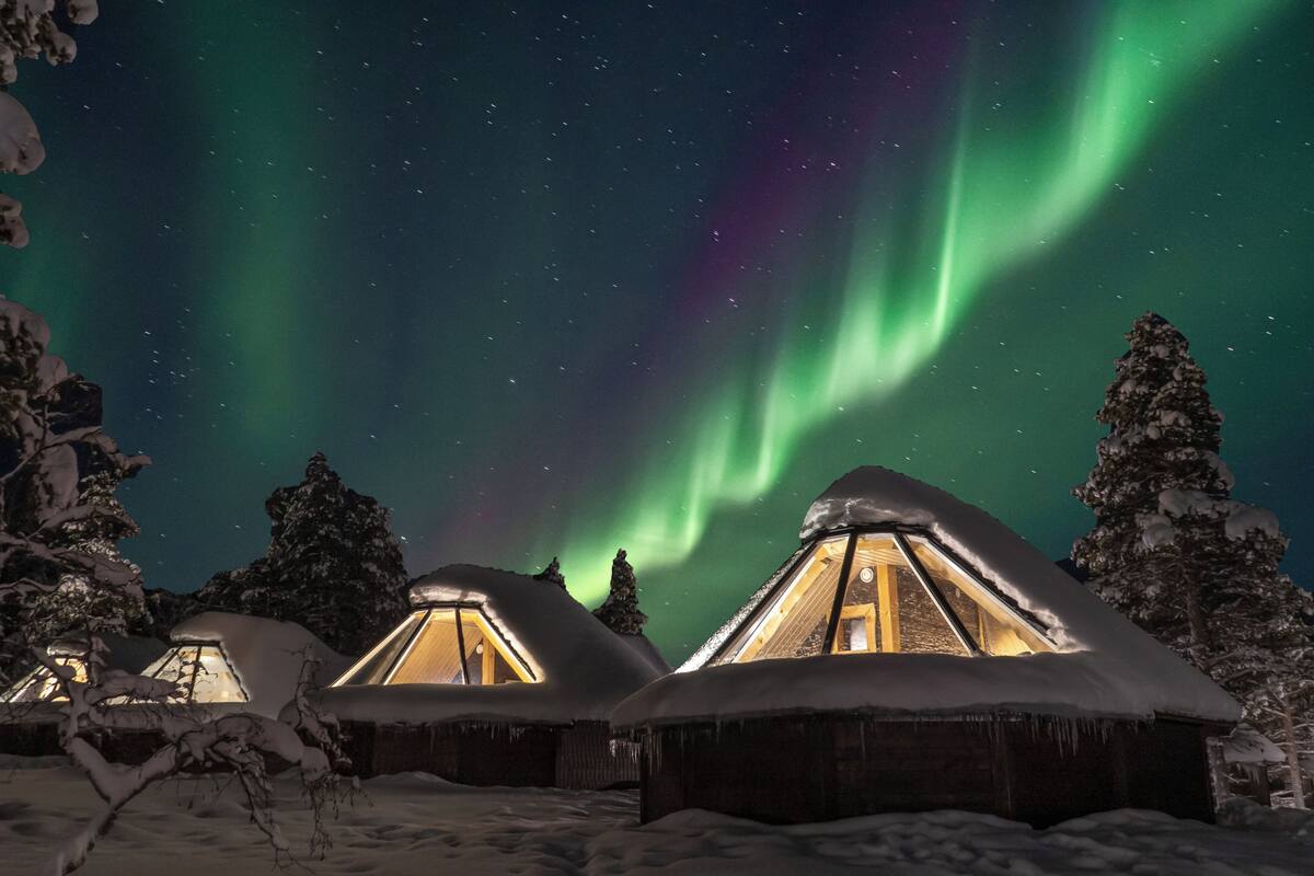 Un paisaje nevado con varias cabañas de madera, cada una con techo triangular y luz interior visible.