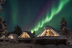A snowy landscape with several wooden cabins, each with a triangular roof and a visible interior light.
