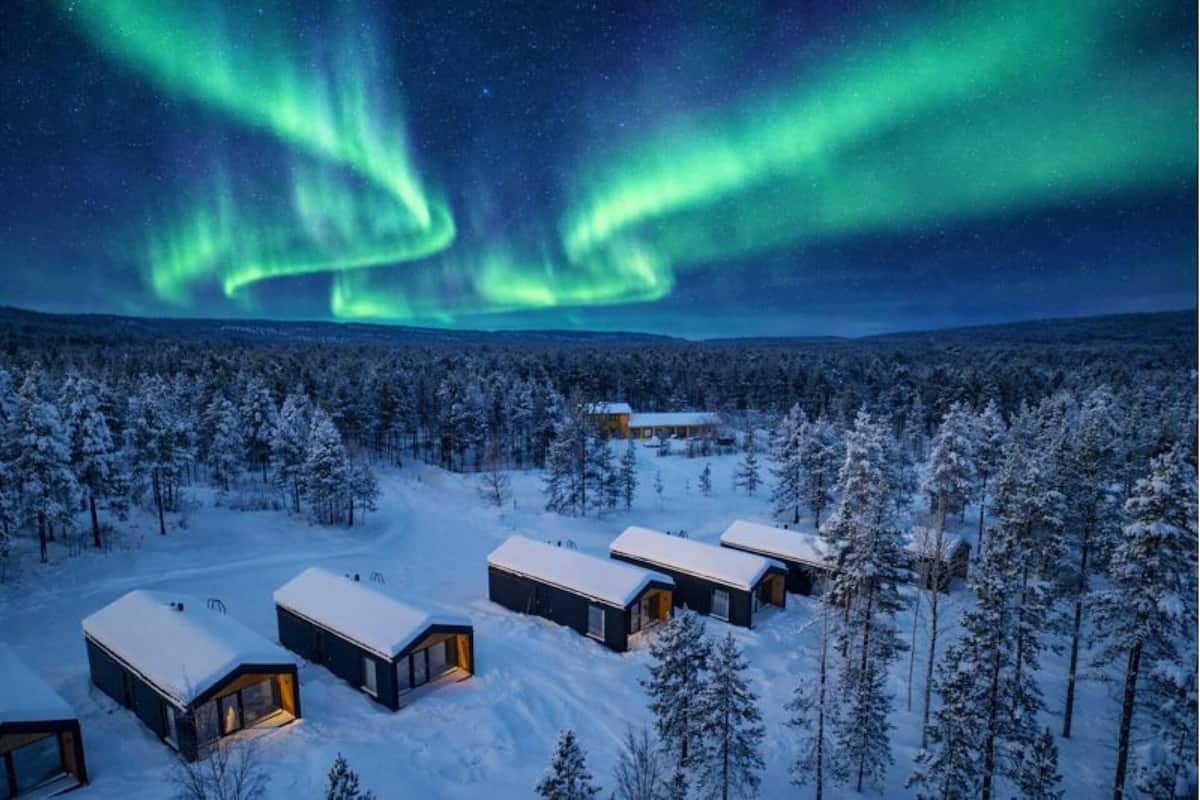Paisaje nevado con varias cabañas y una aurora boreal visible.