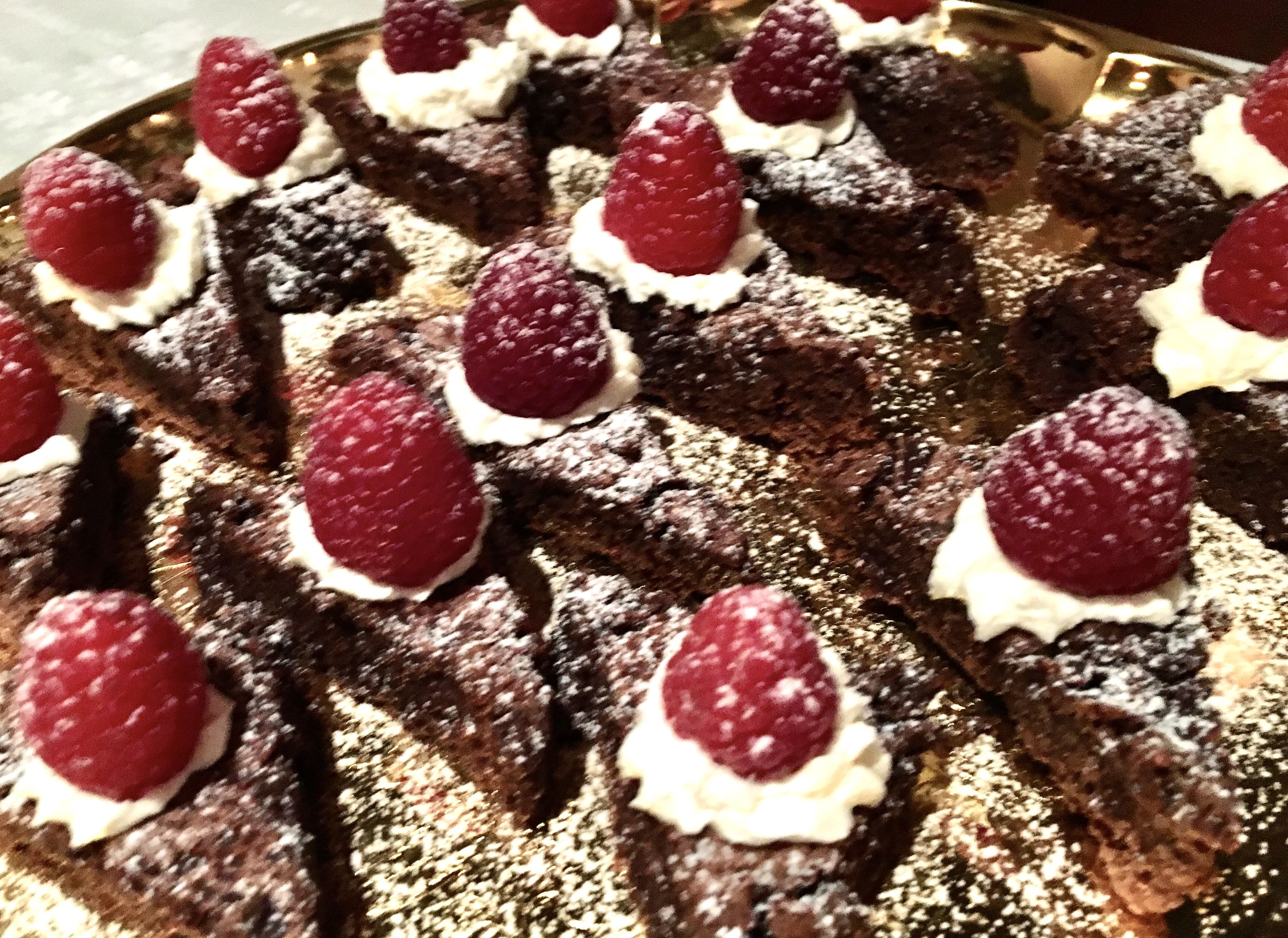 A tray of brownies with whipped cream and raspberries.