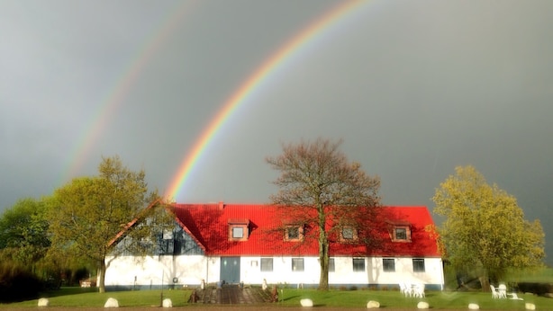 Une maison avec un toit rouge et des murs blancs, entourée d’arbres et d’une pelouse.