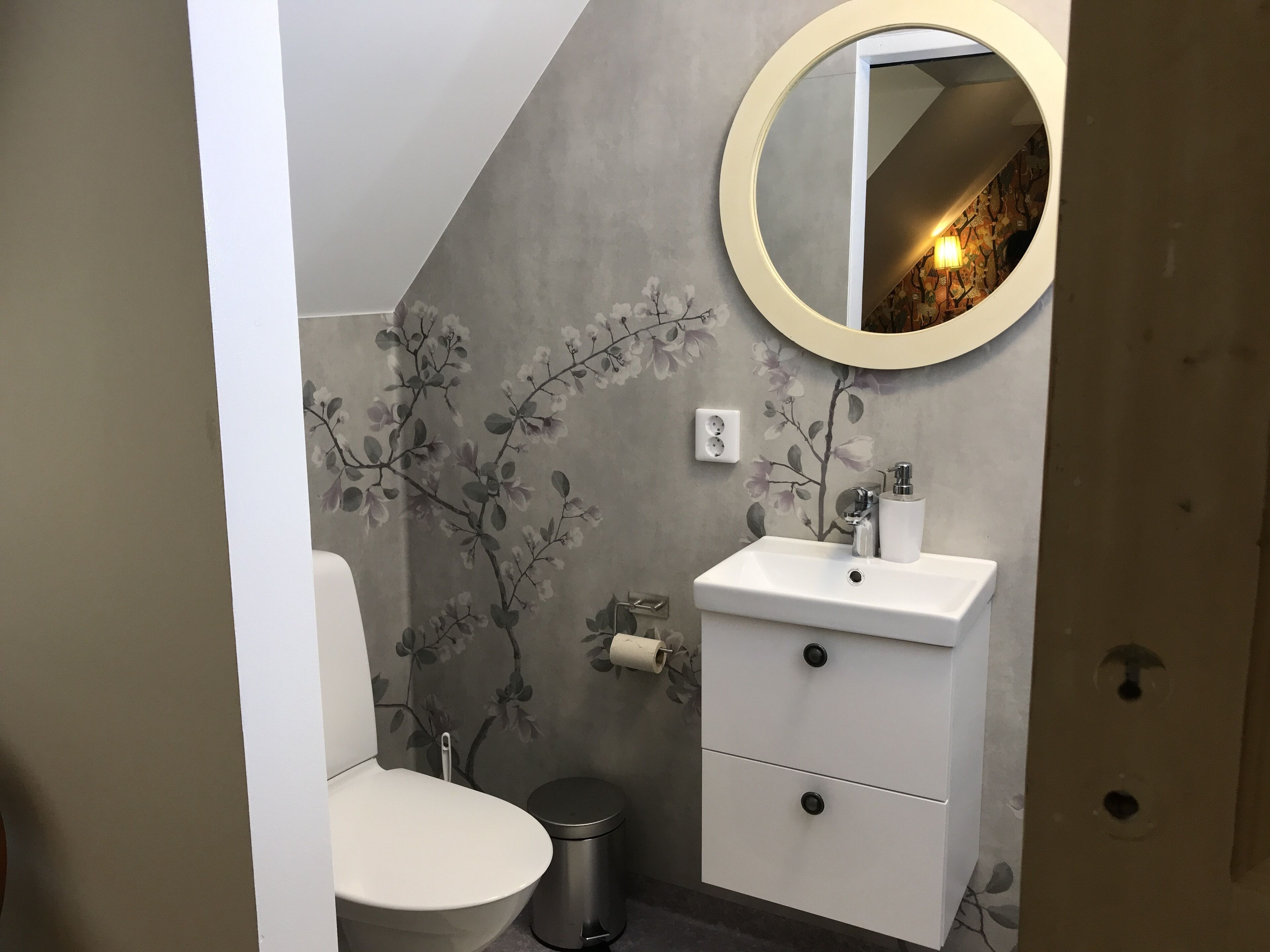 A bathroom with a toilet, a sink, a trash bin, and a mirror.