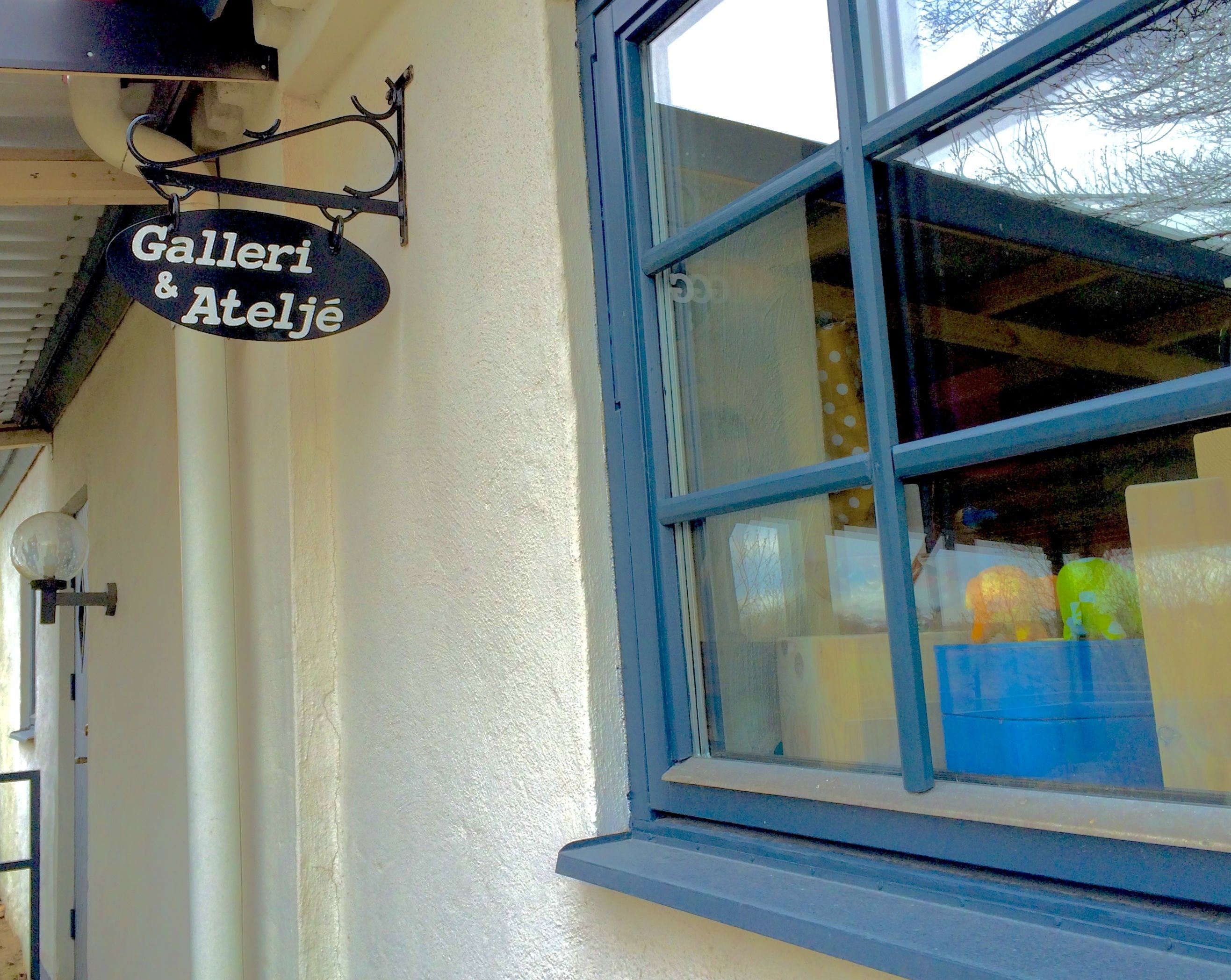 Un escaparate con un letrero que dice "Gallerie & Ateliere" y una ventana que muestra objetos coloridos.