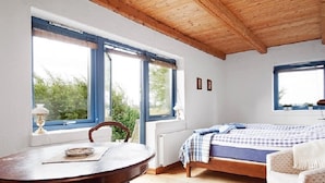 Une chambre avec un plafond en bois, un lit recouvert d’une courtepointe à carreaux, une table avec une lampe et une chaise.