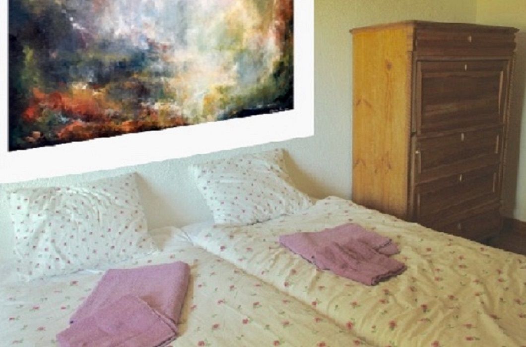 Quarto com cama, almofadas, cômoda e um quadro na parede.