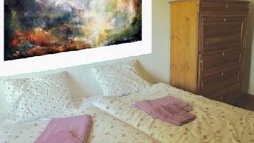 Quarto com cama, almofadas, cômoda e um quadro na parede.