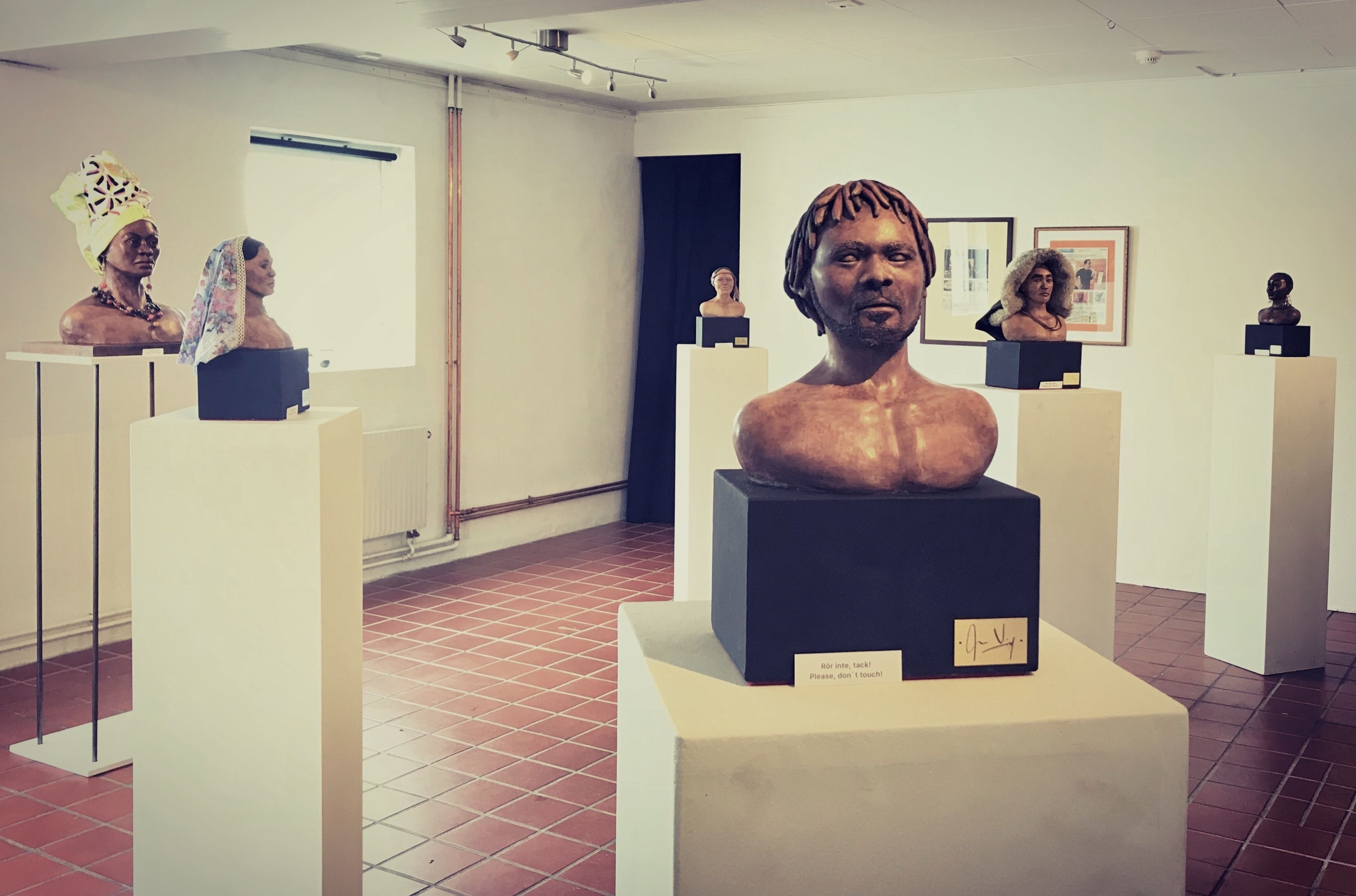 Ett galleri med skulpturer på piedestaler, vita väggar och ett kaklat golv.