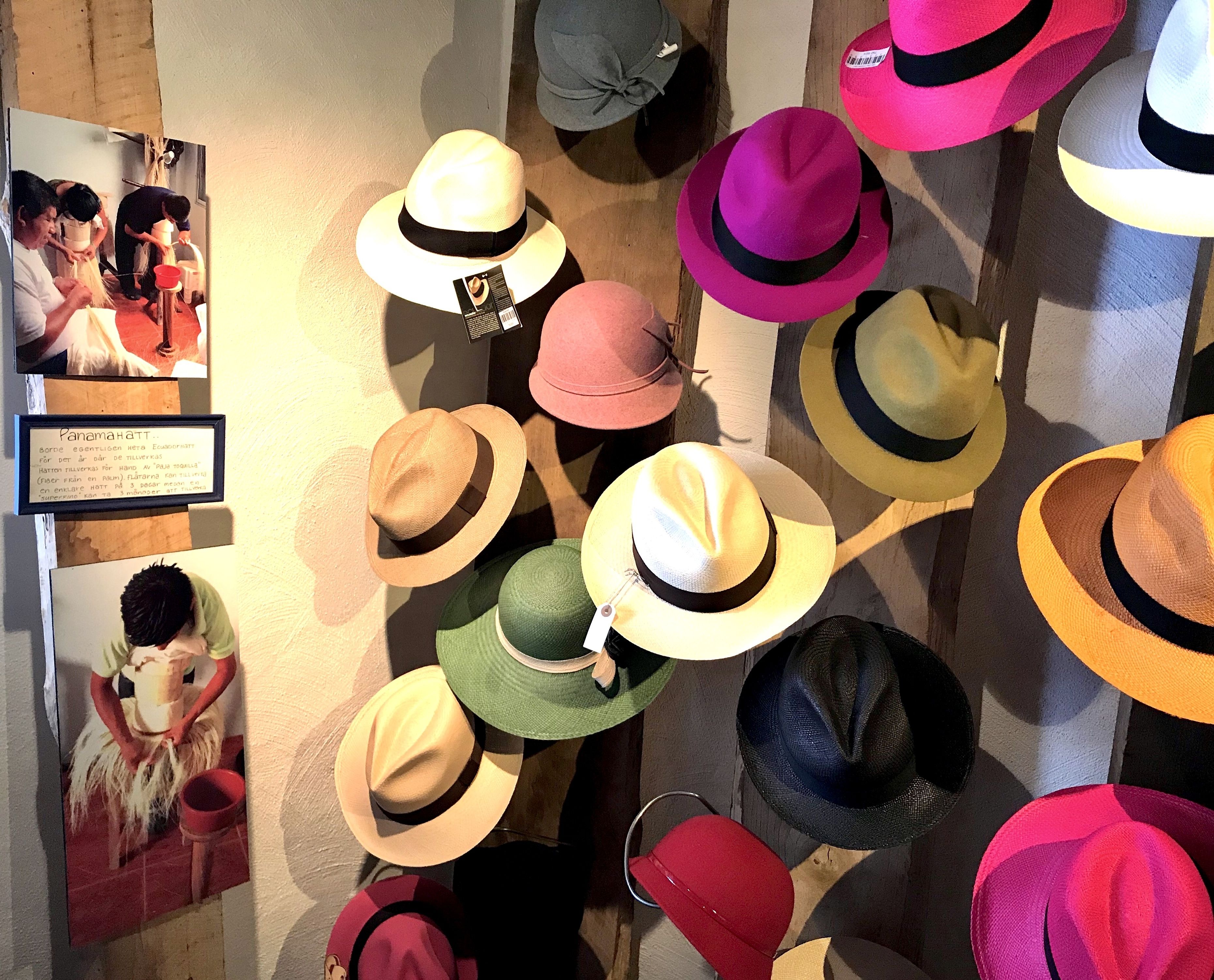Una colección de sombreros exhibidos en una pared, con un cuadro enmarcado de personas vestidas con atuendo tradicional y un letrero con texto.