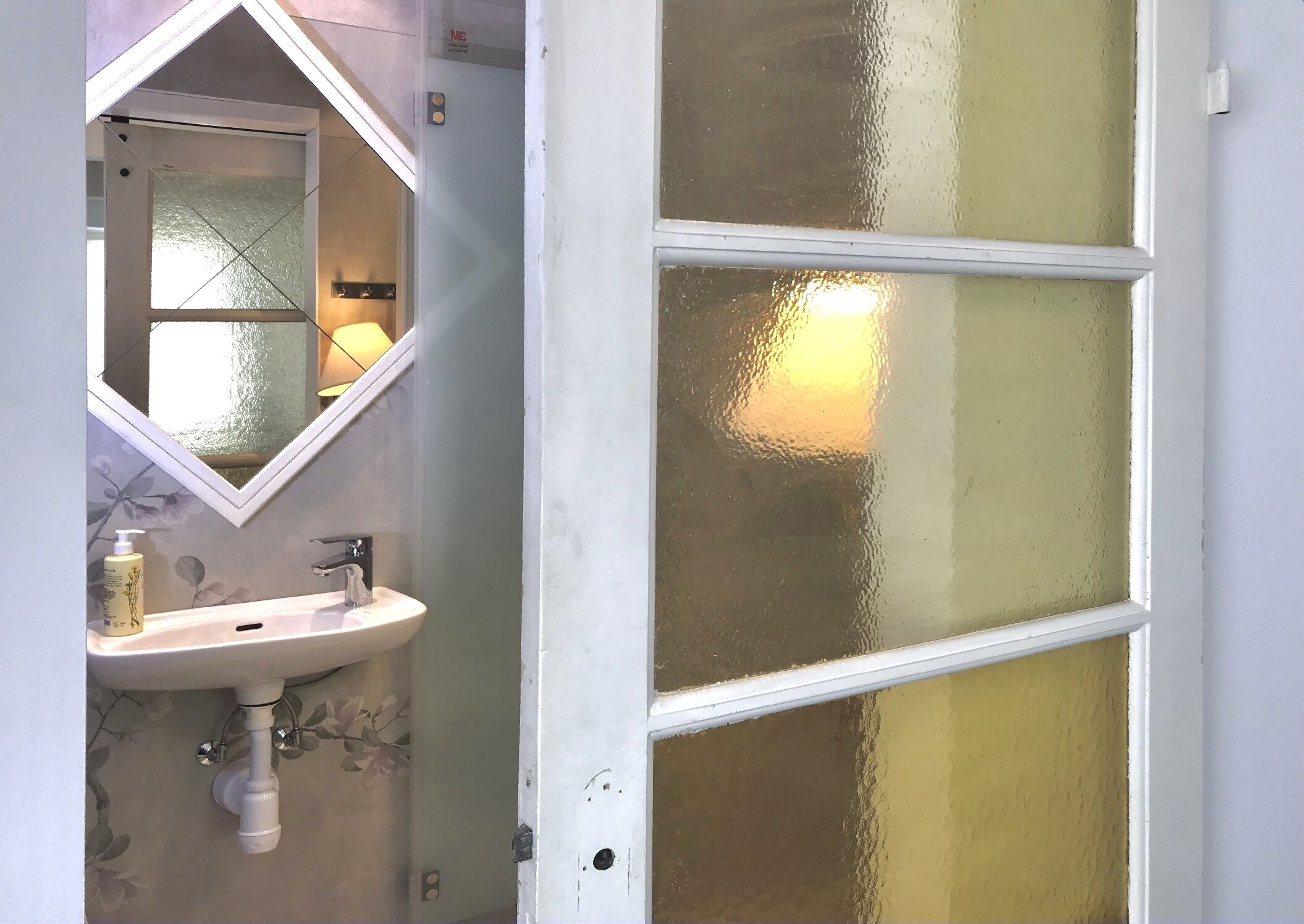 A bathroom with a white sink, a mirror, and a frosted glass door.