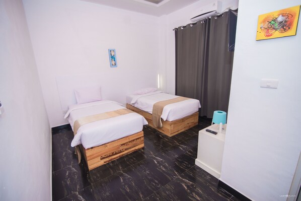 A hotel room with two wooden beds, a white desk, a curtain, and a painting on the wall.