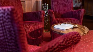 A cozy room with two red patterned armchairs and a small wooden table with an open book and glasses.