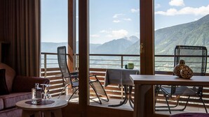 A room with a table and chairs, a sofa, and a view of mountains through large windows. - MARINIs giardino Hotel (Tirolo)