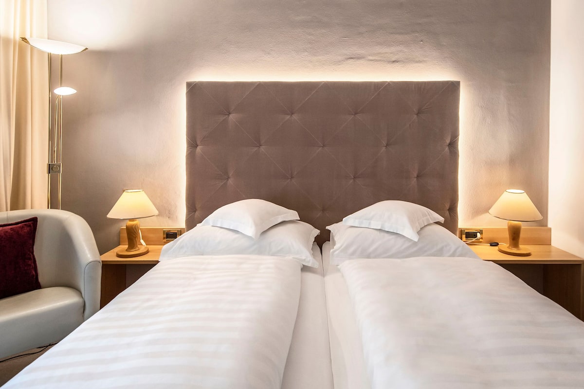 A hotel room with a large bed, two bedside tables with lamps, a chair, and a headboard.