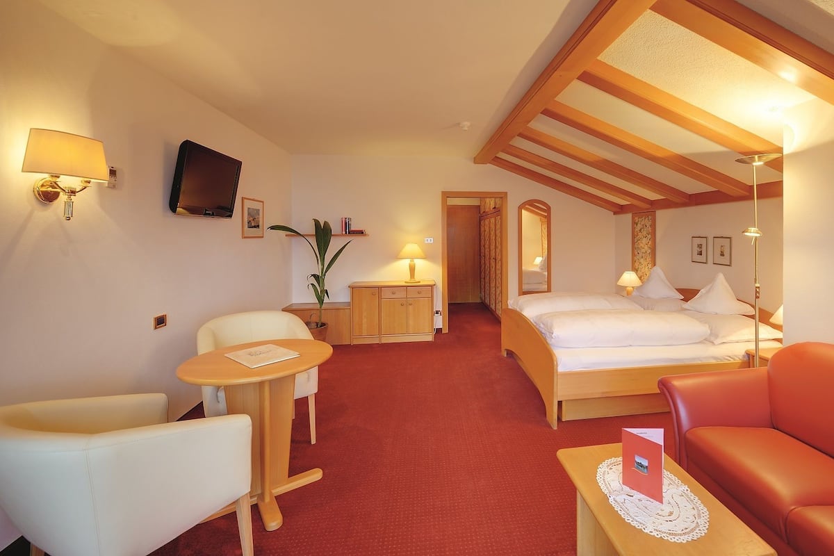 A hotel room with a bed, a desk, a chair, a sofa, and a small table with a decorative item.