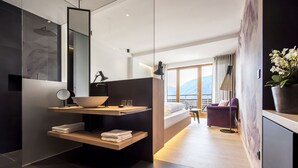 A modern hotel room with a large bed, a vanity with a bowl sink, a mirror, and a potted plant. - MARINIs giardino Hotel (Tirolo)