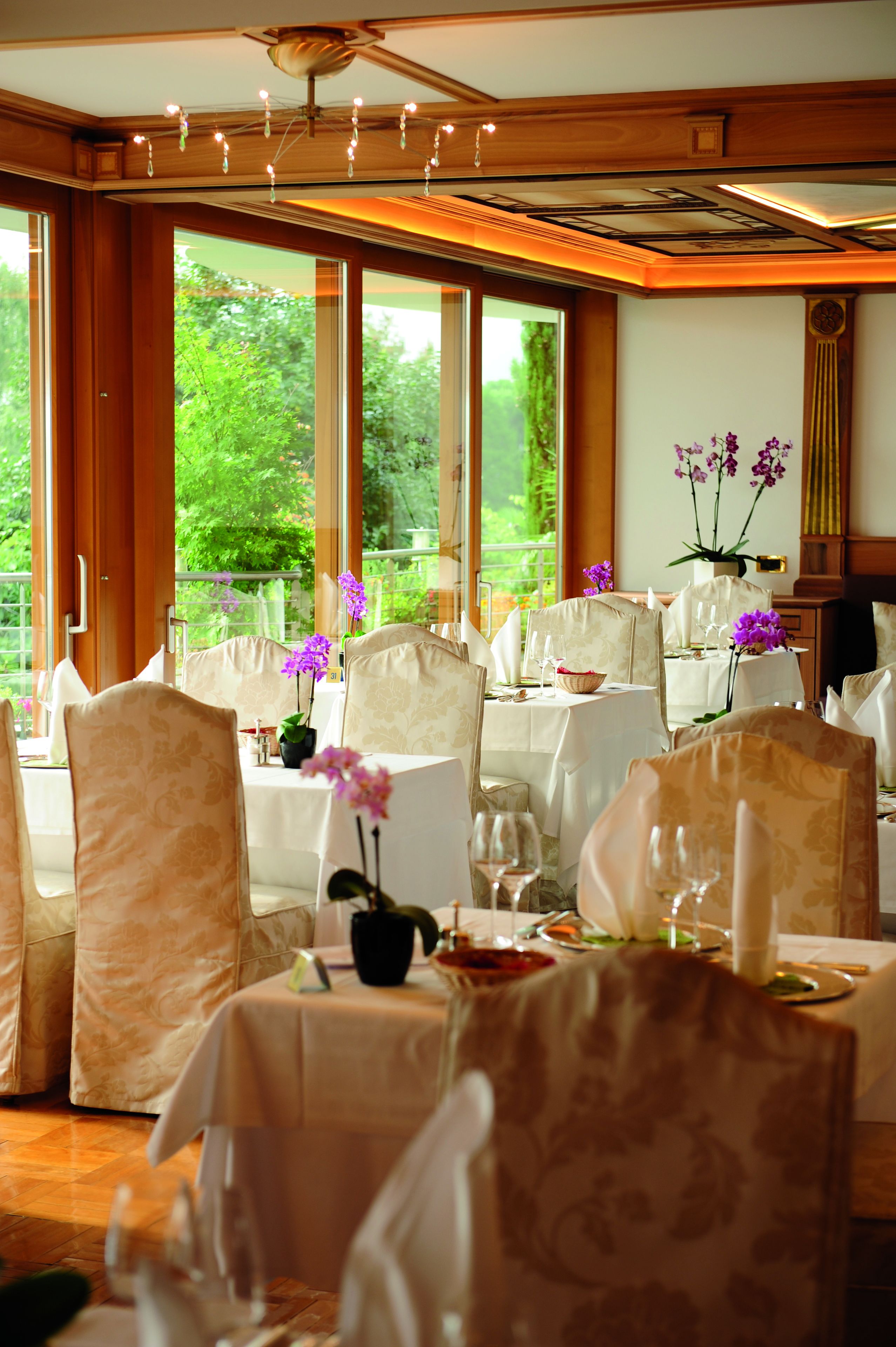 A dining area with tables set for a meal, chairs, and a view of greenery outside.
