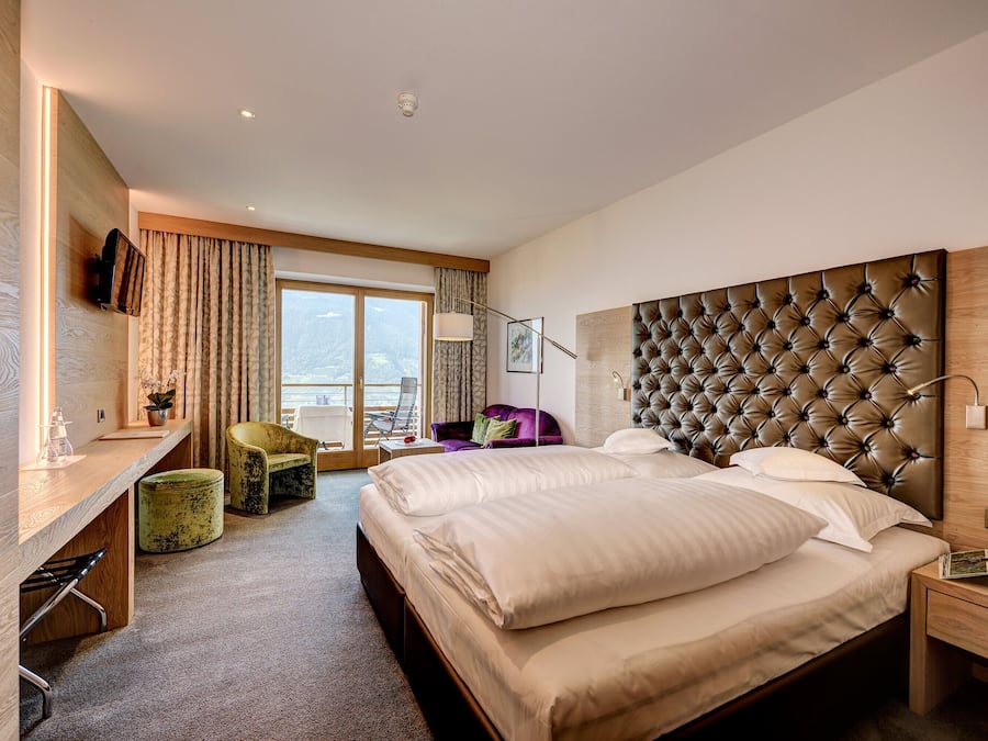 Ein modernes Hotelzimmer mit einem großen Bett, einem Schreibtisch, einem Sessel und einem Balkon mit Aussicht.