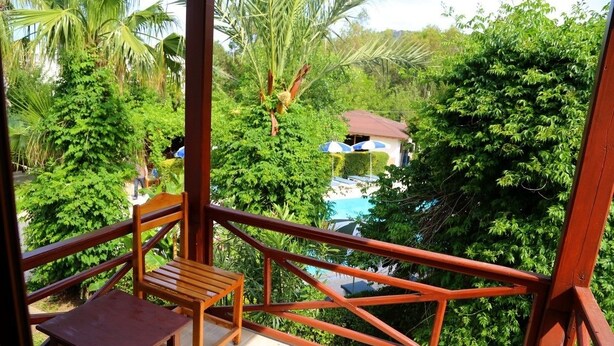 A wooden deck with a table and chairs, overlooking a lush green landscape with a pool and a building in the background. - Arkadas Otel (Kumluca)