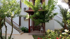 A covered outdoor seating area with a staircase leading to a building, surrounded by greenery and flowering plants. - Arkadas Otel (Kumluca)