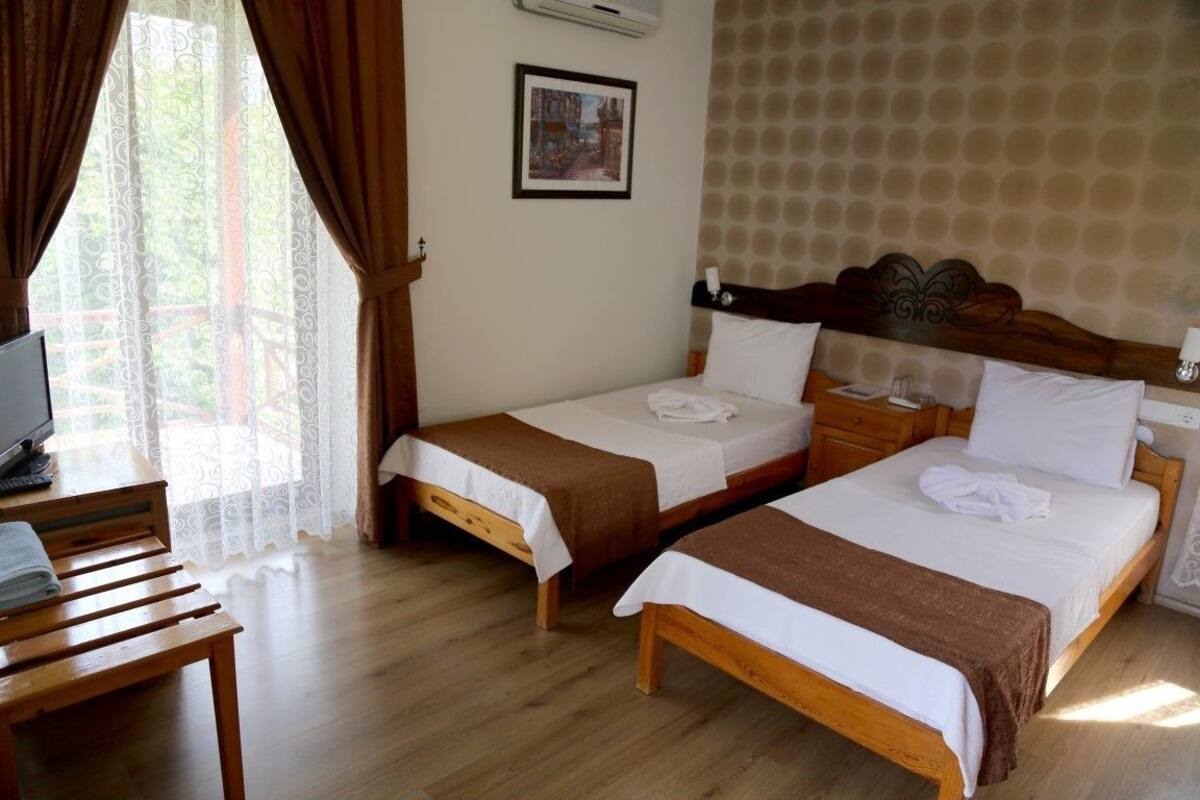 A hotel room with two single beds, a wooden desk, a television, and a window with curtains.