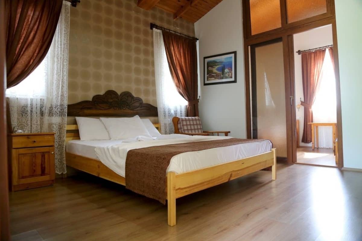 A wooden bed in a room with a patterned wall, a wooden nightstand, and a chair.