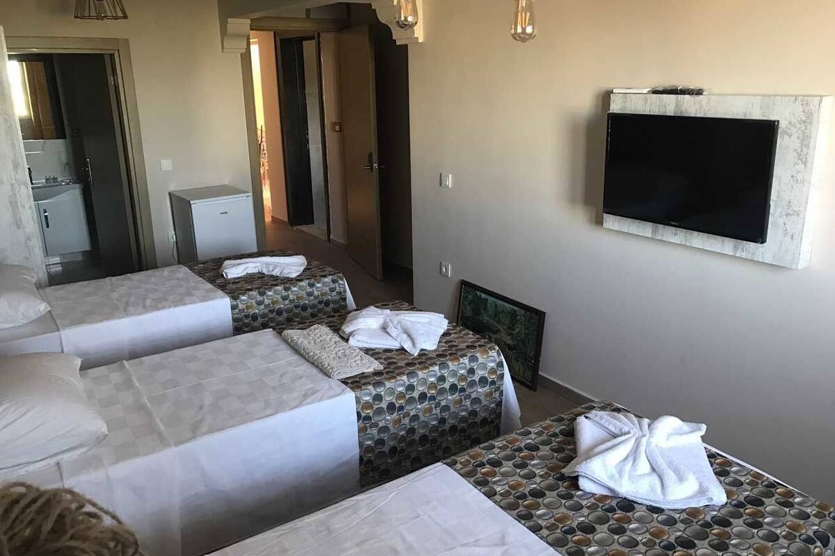 A hotel room with three beds, a flat-screen TV mounted on the wall, and a small kitchenette area.