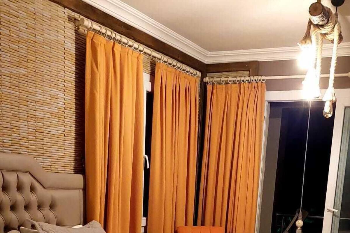 A bedroom with a large bed, orange curtains, and a view of the outside.