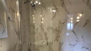 Ein modernes Badezimmer mit einer gläsernen Duschkabine, Marmorfliesen und einem weißen Waschbecken.