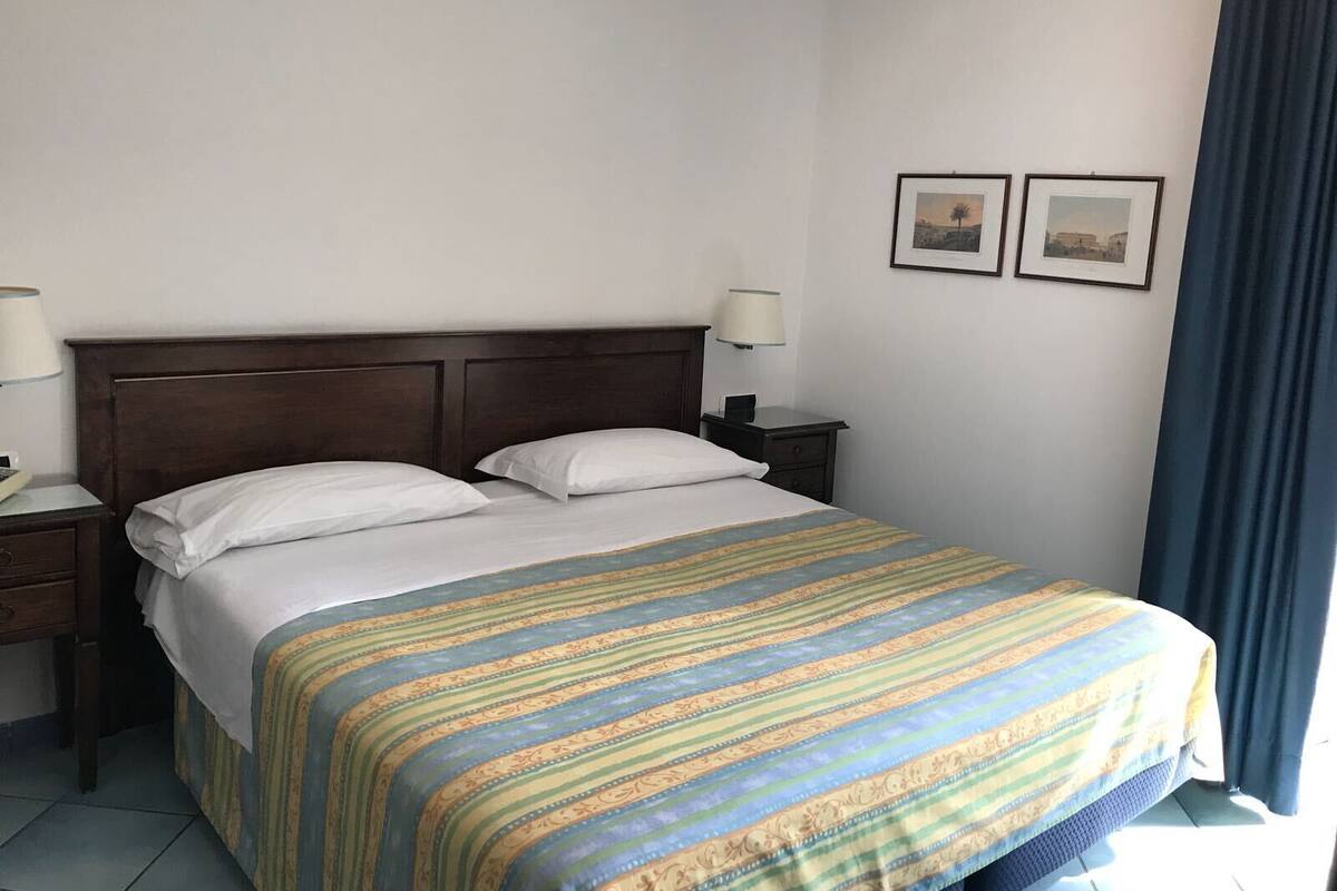 A hotel room with a large bed, two bedside tables, and two wall-mounted lamps.