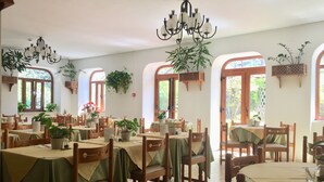 Um restaurante com várias mesas e cadeiras, plantas em vasos e plantas penduradas.