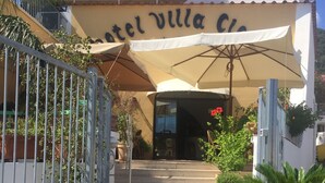 Entrada de hotel com uma placa indicando "Hotel Villa Cie" e uma área de acesso coberta, com degraus que levam à porta.