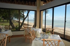 A dining area with tables set for two, overlooking a beach with palm trees and a clear view of the ocean. - Jumuia Conference & Beach Resort (Mtwapa)