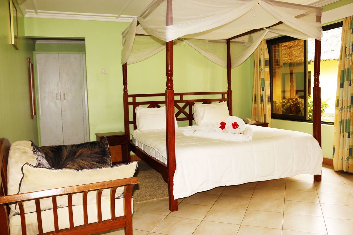 A four-poster bed with a canopy, a wooden chair, and a door in a room with green walls and tiled flooring.