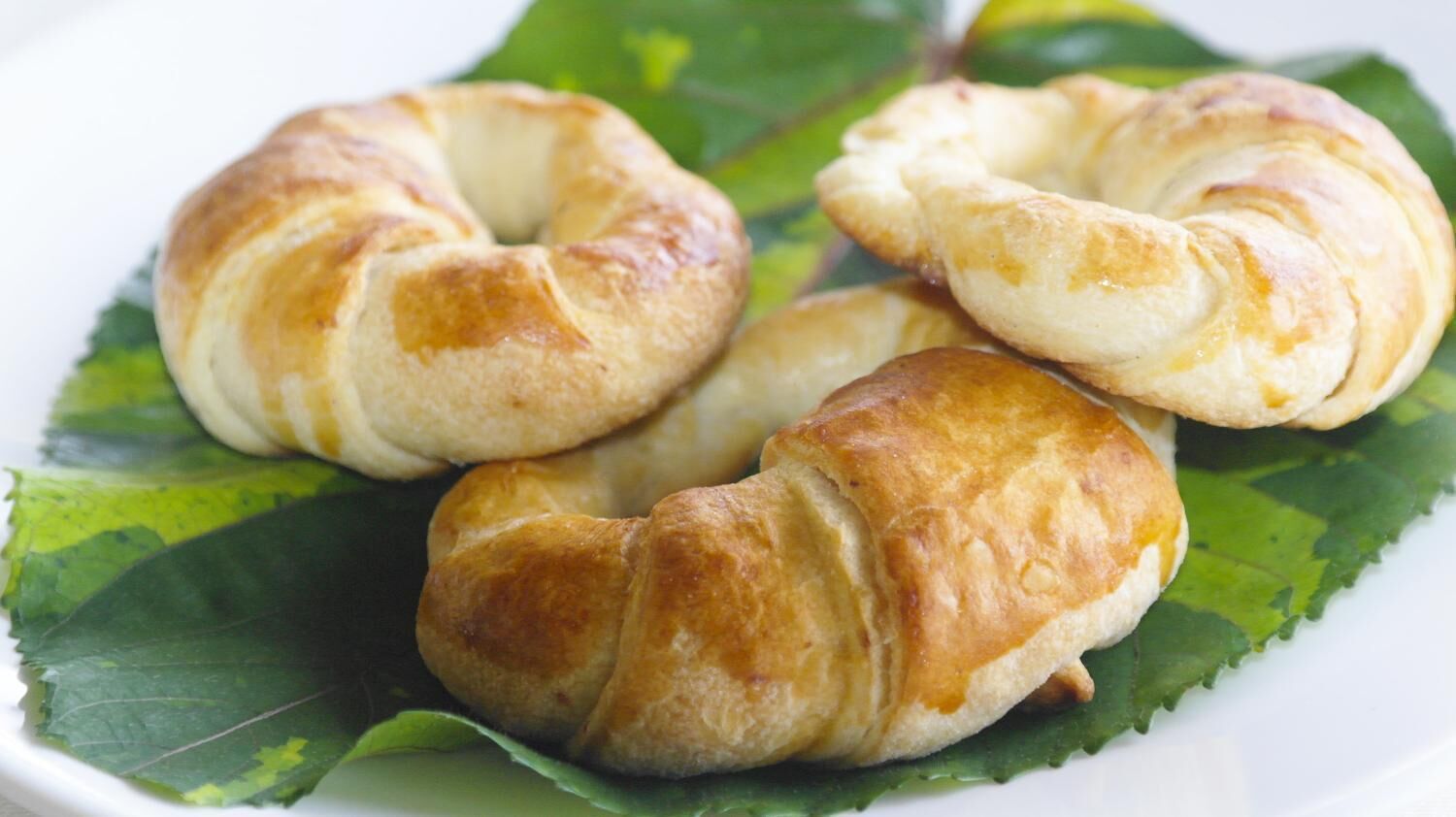 Three croissants on a white plate with a green leaf underneath.
