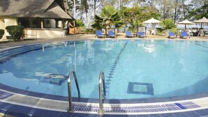 A swimming pool with blue lounge chairs and a thatched-roof building in the background. - Jumuia Conference & Beach Resort (Mtwapa)