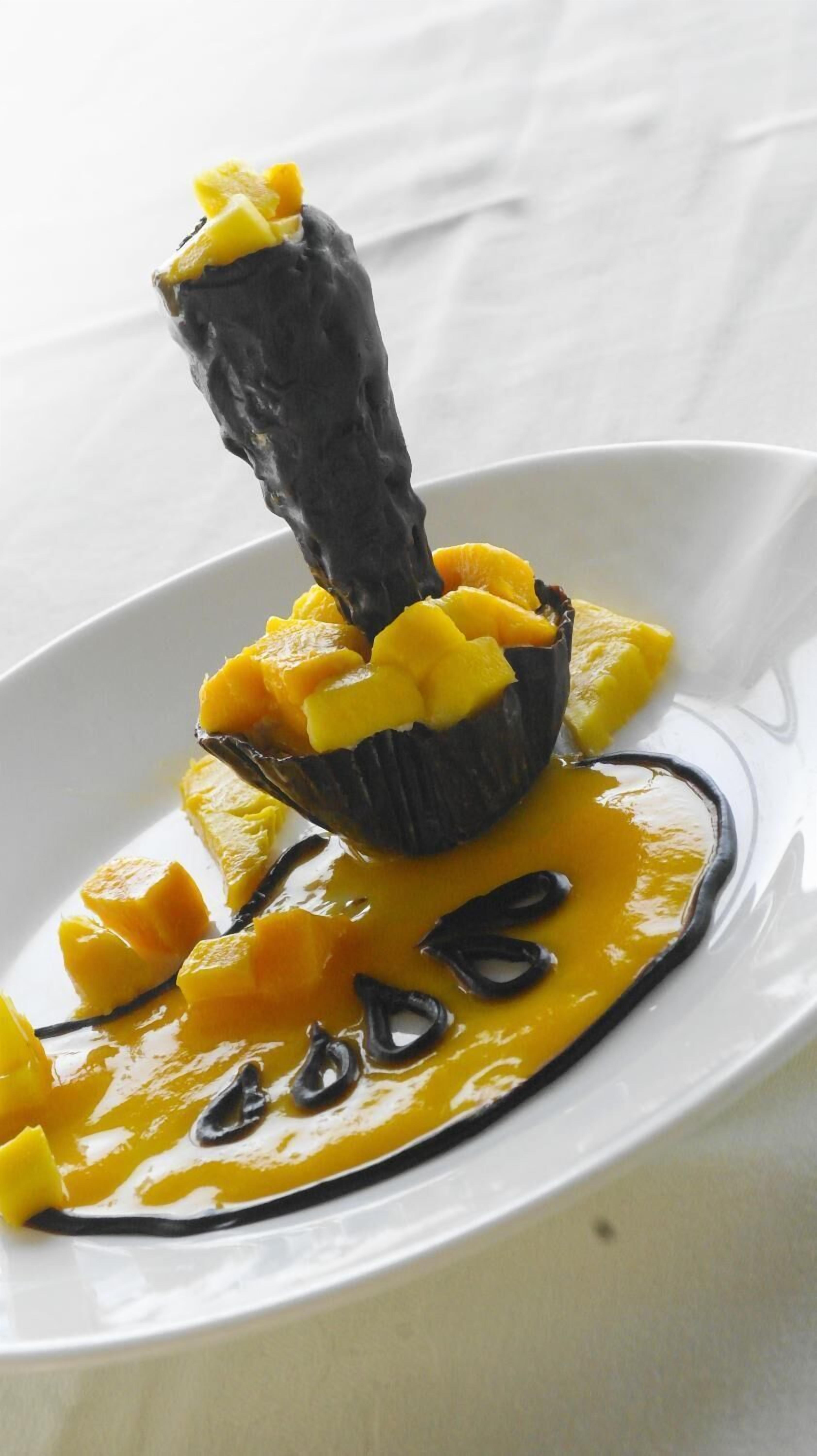 Uma sobremesa com cobertura escura e brilhante e pedaços de fruta amarela em um prato branco.