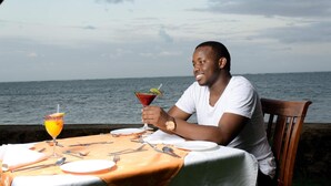 A person seated at a table with a view of the sea, holding a cocktail glass. - Jumuia Conference & Beach Resort (Mtwapa)