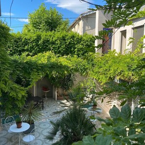 A courtyard with a tiled floor, a table with chairs, and various potted plants. - Couette et Cafe (Montpellier)