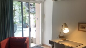 A room with a red armchair, a desk with a lamp, and an air conditioning unit on the wall.