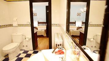 A bathroom with a checkered floor, a toilet, a sink with a mirror, and a bed visible through an open door.