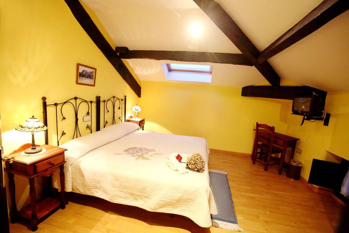 A bedroom with a bed, bedside lamps, a small table, a chair, and a television.