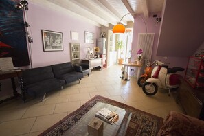 A living room with a sofa, a coffee table, and a motorcycle. There are framed pictures on the wall and a lamp.