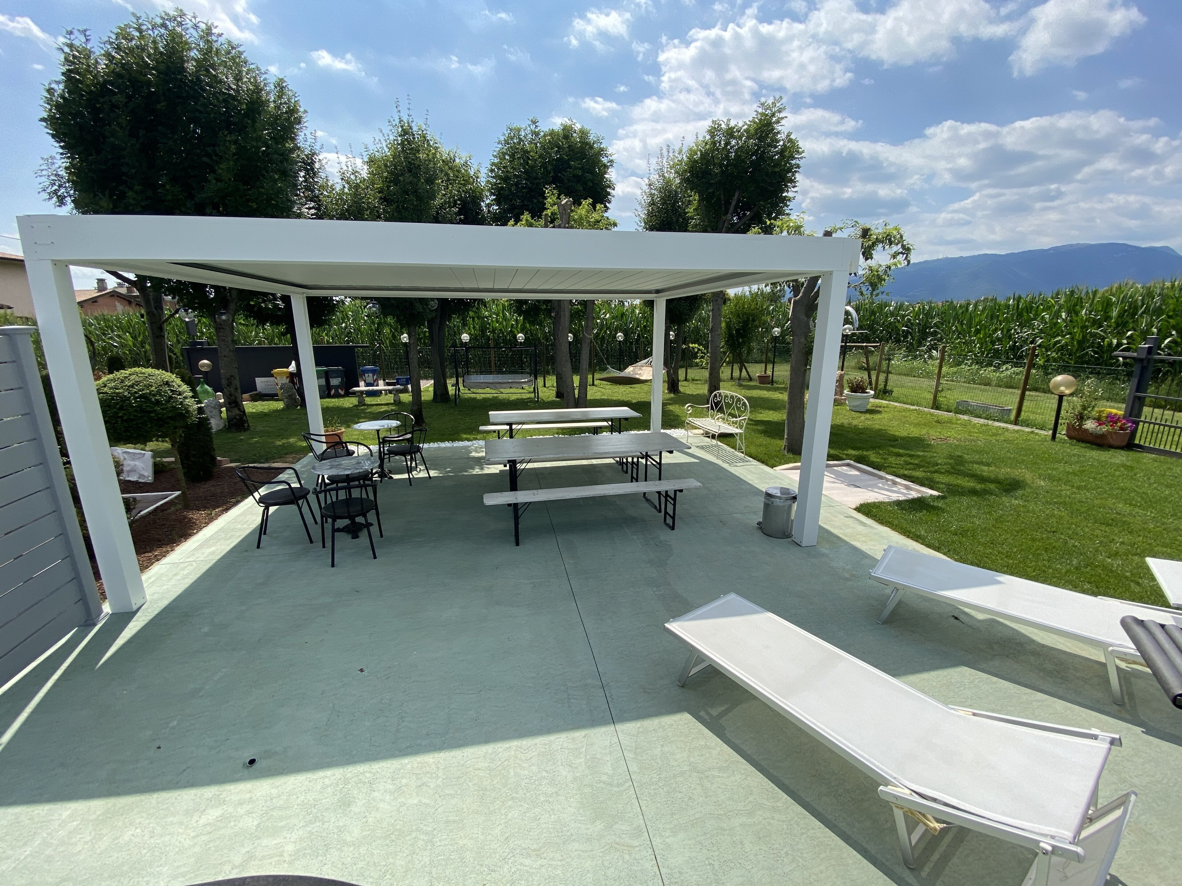 A covered outdoor patio with tables and benches, surrounded by greenery and a view of distant mountains.