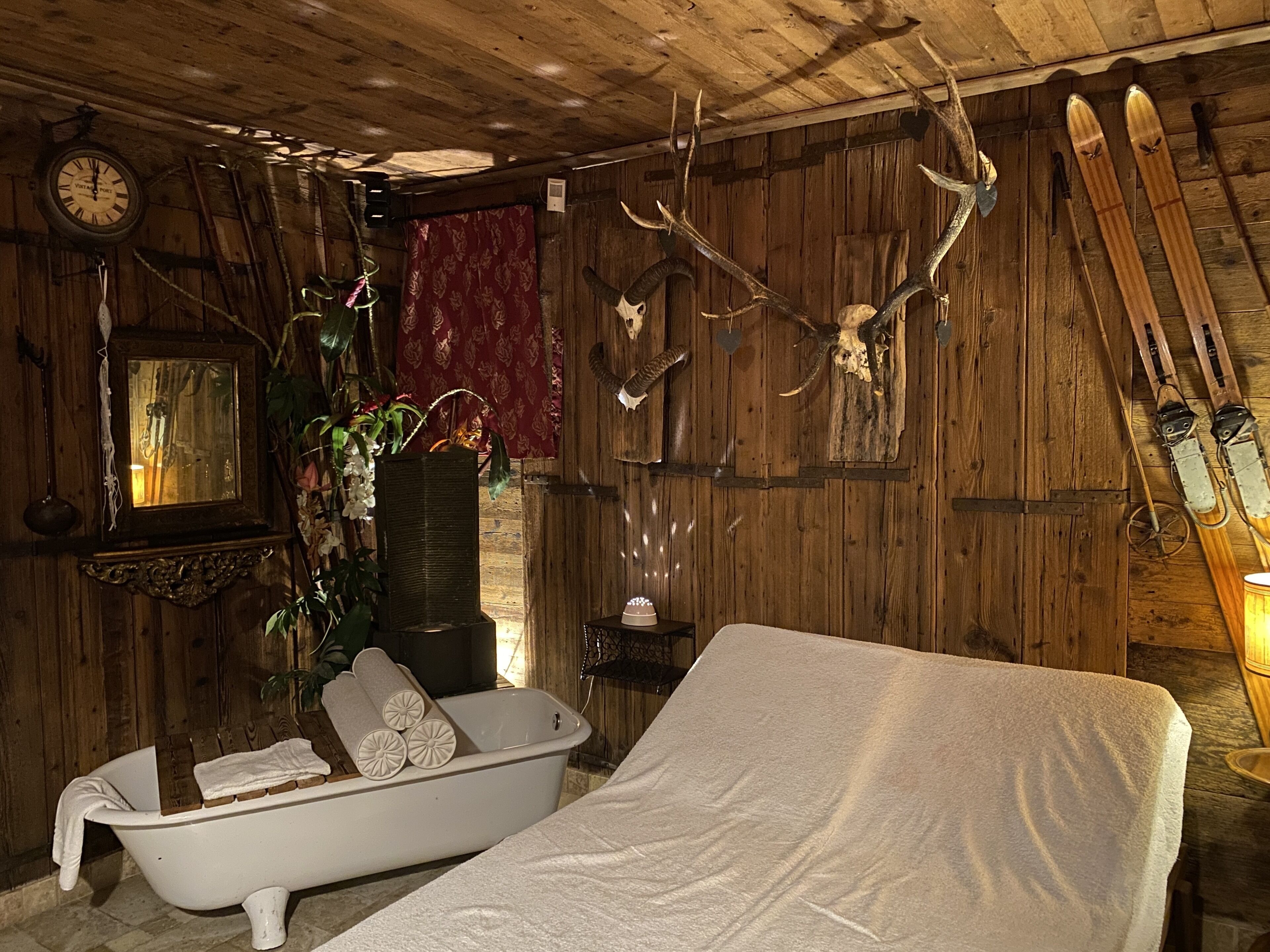 A rustic room with a wooden interior, a white bathtub, skis, and antlers on the wall.