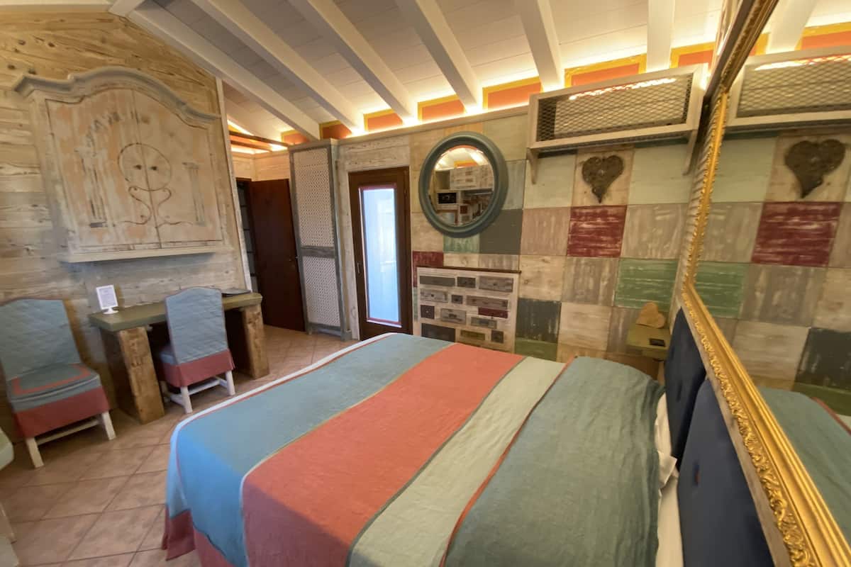 Une pièce comprenant un lit, un bureau et une chaise. Il y a un miroir au mur et une fenêtre avec des stores.