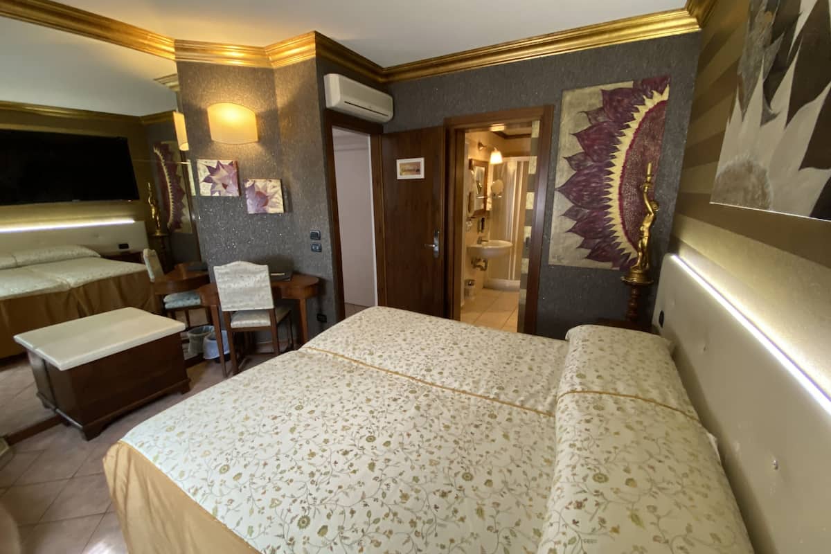 Une chambre d’hôtel avec un grand lit, un bureau avec une chaise, une petite table et une coiffeuse avec un miroir.