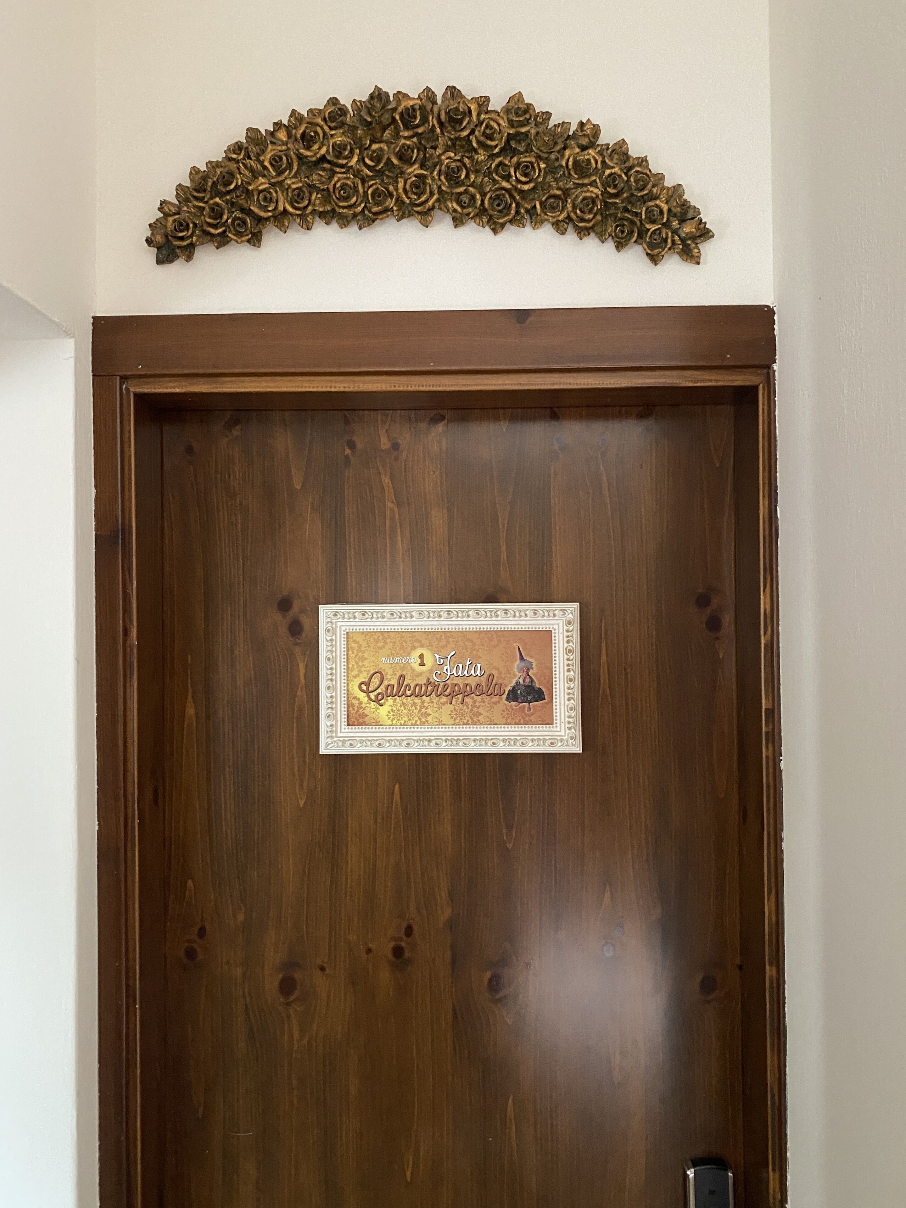 A wooden door with a brass floral decoration above it and a sign with a cartoon character.