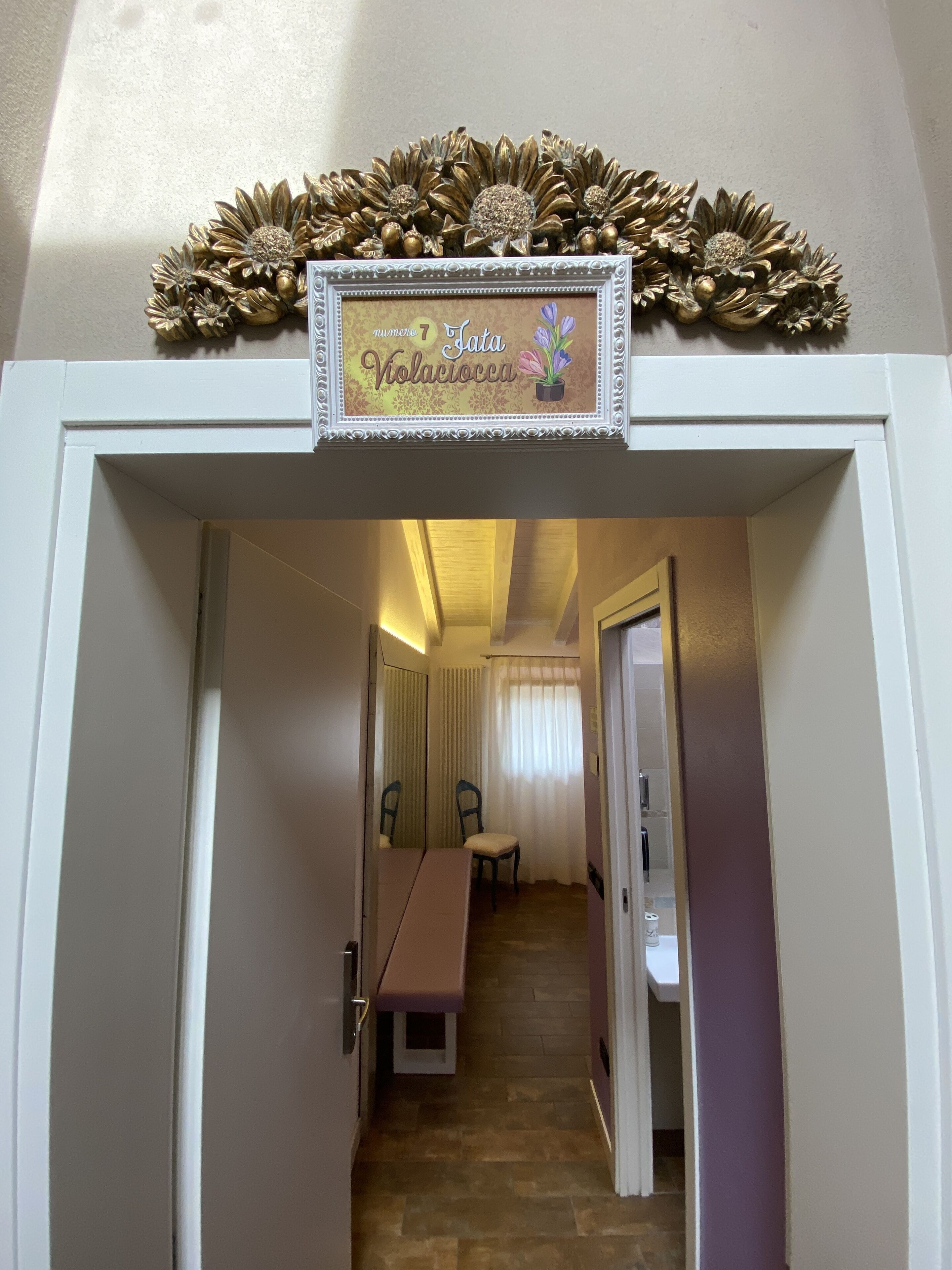 A hallway leading to a dining area with a table and chairs, a mirror, and a decorative sign above the door.